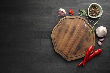 Wall Mural - Cutting board, spices, garlic, rosemary and chili peppers on black wooden table, flat lay. Space for text