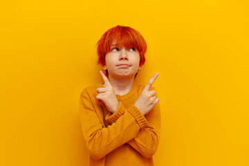 uncertain red-haired teenage boy chooses between two options and points with his fingers on yellow isolated background, confused child with orange hairstyle thinks and points with his hands at copy