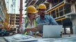 © Mahemud - Two colleagues discussing data working and tablet, laptop with on on architectural project at construction site at desk in office