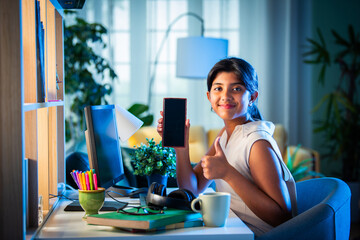 Wall Mural - Indian asian teenage school girl studying online at home using smartphone and computer