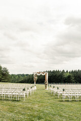 Wall Mural - Outdoor wedding ceremony with floral arch and rows of white chairs=