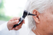 © manassanant - Otolaryngologist or ENT physician doctor examining senior patient ear with otoscope, hearing loss problem.