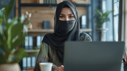 Wall Mural - The gorgeous Muslim businesswoman wearing a burka is sitting at her desk working on her laptop computer in the office. The successful corporate CEO plans an investment strategy for an e-commerce