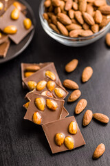 Wall Mural - Broken chocolate bar with almonds on black table.