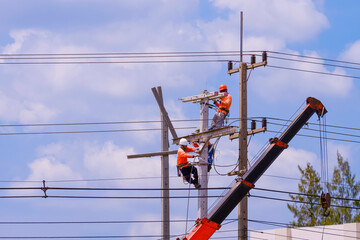 Electricians team with crane truck are working to install electrical equipment on new electric power poles against blue sky background