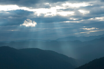 Wall Mural - Sun rays filter through the clouds in hills of the valley illuminated by the sun's rays filtering through the clouds