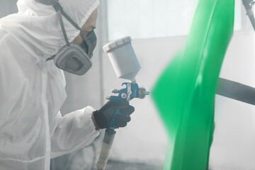 Wall Mural - Car repair painter in protective overalls and painting a respirator part of car in the paint chamber