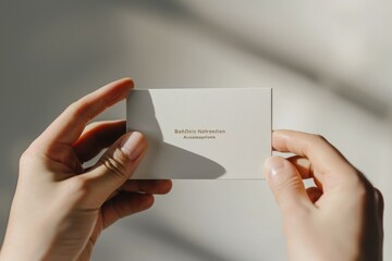 Wall Mural - A closeup of a person holding a business card elegantly between their fingers against a neutral background