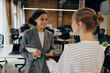 © Daria - Two young diverse business women chatting during work break standing in modern office