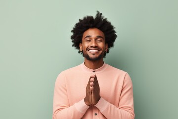Sticker - Portrait of a smiling afro-american man in his 20s joining palms in a gesture of gratitude isolated in solid pastel color wall