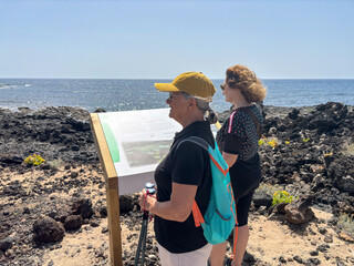 Sticker - Outdoor activity in nature concept. Couple of sporty women friends enjoying healthy lifestyle hiking along a rocky beach in southern Tenerife stops to read touristic informations.