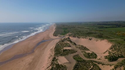 Wall Mural - aerial orbit over grassy sand dunes, slowly revealing wind turbines generating energy offshore