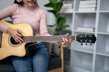 Wall Mural - A woman is playing a guitar in a room with a lot of books. The room has a cozy and comfortable atmosphere