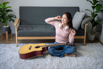 Wall Mural - A woman is sitting on the floor with a guitar in front of her. She is wearing headphones and she is enjoying herself