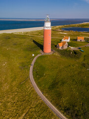 Wall Mural - A stunning aerial view of a lighthouse standing tall near the ocean, surrounded by vast blue waters and endless skies, offering guidance and safety to passing ships.
