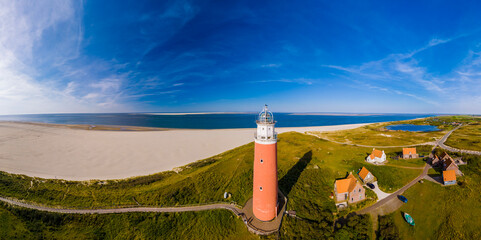 Poster - An aerial perspective of a lighthouse standing tall on the sandy beach, overlooking the vast expanse of the ocean with its beacon shining brightly. The iconic red lighthouse of Texel Netherlands