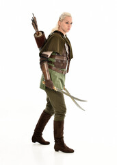 Poster - full length portrait of blonde female model wearing green fantasy elf warrior halloween costume with leather armour. standing pose, holding weapons.  isolated on white studio background.