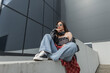 © alones - Fashion beauty cool hipster woman with headphones with sunglasses in casual clothes with bandana, jeans and sneakers sits on the street