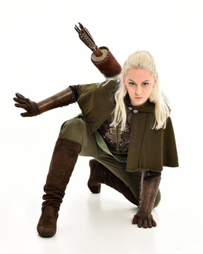 full length portrait of blonde female model wearing green fantasy elf warrior halloween costume with leather armour. sitting pose kneeling. isolated on white studio background.