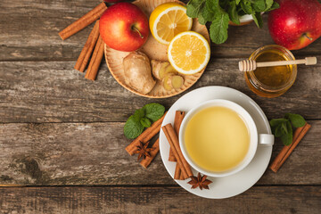 Wall Mural - Fragrant hot tea with cinnamon stick and anise on a textured wooden background. A cup of hot tea with honey, lemon, mint and apples. Spicy tea with spices. Immunity tea. Health concept.Copy space.