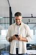 © Stock 4 You - Vertical portrait of middle aged Hispanic business manager using cell phone mobile app. Smiling Latin or Indian mature man businessman holding smartphone standing in office, working online on gadget.