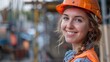 © MINHO - Portrait of beautiful female building construction technician architect wearing helmet and orange high visibility vest, smiling at work site. Manufacturing technology work concept.