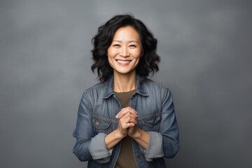 Sticker - Portrait of a smiling asian woman in her 40s joining palms in a gesture of gratitude in front of blank studio backdrop