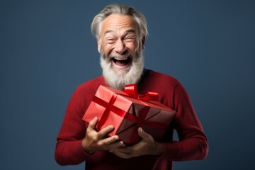 Wall Mural - Portrait of a joyful man in his 50s holding a gift on blank studio backdrop
