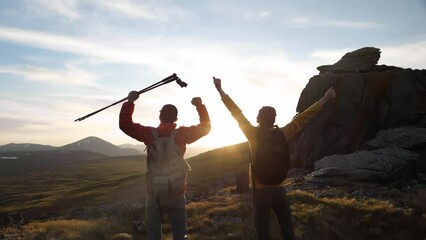 Aufkleber - Two happy young tourists are standing in happy winner poses with open arms against sunset sky and mountains