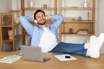 Aufkleber - A man is seated at a desk, wearing headphones and working on a laptop placed on his lap. He appears focused and engaged in his work, with various papers and stationery scattered around the desk.
