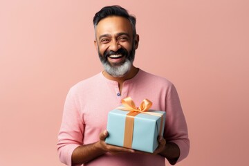 Wall Mural - Portrait of a satisfied indian man in his 40s holding a gift over light wood minimalistic setup