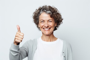 Wall Mural - Portrait of a happy woman in her 50s showing a thumb up while standing against plain white digital canvas