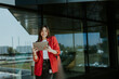 © BGStock72 - Smiling businesswoman in red blazer using tablet at modern office window in daylight