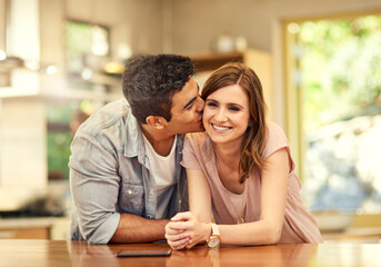 Canvas Print - Couple, people and happy with kiss in kitchen for love, bonding and affection with support on break together. Home, relationship and romance with smile or laugh for fun, enjoy and care as soulmate