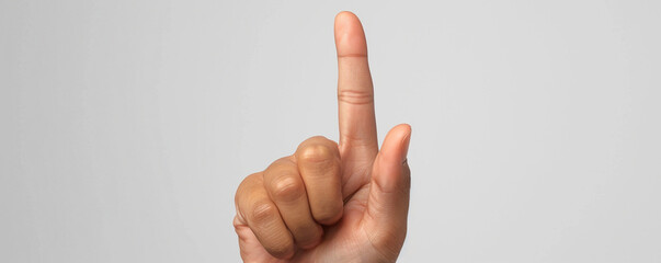 Close-up of a hand with one finger raised against a plain grey background. Excellent for concepts of communication, counting, or signaling.