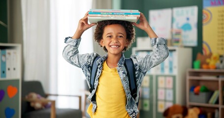 Poster - Child, face and book on head in school classroom for education learning in kindergarten, scholarship or happy. Kid, smile and knowledge academy for student creativity as reading, lesson or library