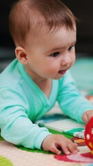 Poster - Curious Caucasian baby boy lying on the floor reaching a ball. Sweet kid takes a toy and bangs it by the floor. Vertical video