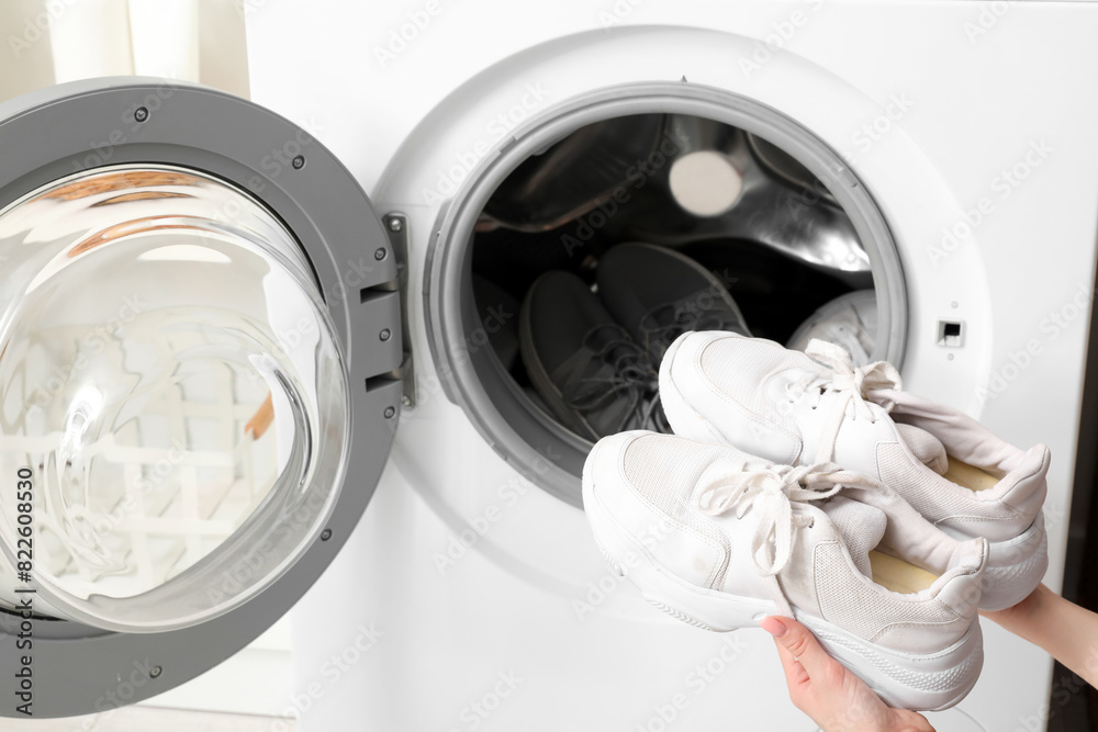 Female hands with sneakers and open washing machine, closeup