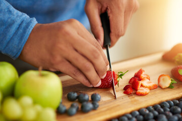 Fruits, hands and healthy food in kitchen for breakfast salad with knife and cutting board. Person or nutritionist with strawberry for wellness, diet and detox with vegan and organic recipe at home