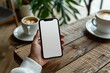 © Sandu - Person holding phone with white screen on wooden table