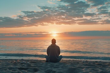 A man is sitting on the beach, looking out at the ocean