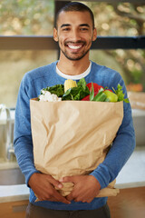 Man, portrait and grocery shopping in kitchen with vegetables and healthy food at home. Happy African person or nutritionist with paper bag for organic cooking, diet or health with sustainable living