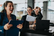© qunica.com - Happy business team celebrating success with documents in hand in a modern office setting. Joyful expressions, teamwork, and professional attire.