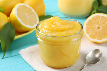 Wall Mural - Delicious lemon curd in glass jar, fresh citrus fruits and spoon on light blue wooden table, closeup