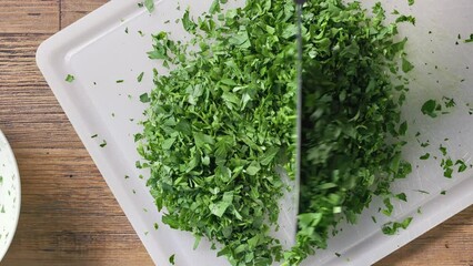 Poster - Chef chops fresh green parsley leaves on white cutting board to prepare healthy food, top view. Food close up