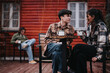 © qunica.com - A young couple shares a moment over cups of coffee on a wooden porch, with a relaxed ambience and a person reading in the background.