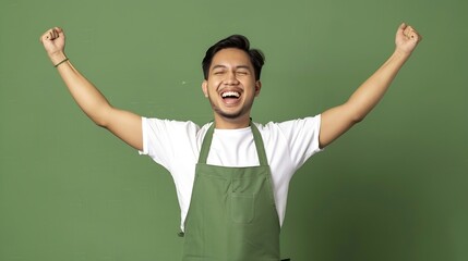 Poster - A portrait of an Indonesian Asian man wearing a white barista tshirt and a green apron looking happy and posing confidently isolated on a green background : Generative AI