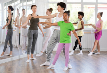 Wall Mural - Focused African American teenage girl carefully practicing ballet moves and basic lifts paired with boy in children dance studio run by female instructor, along with other students