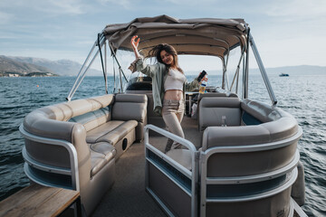 Wall Mural - A happy, joyful girl raises her arms in celebration while standing on a pontoon boat, surrounded by beautiful mountain and water landscapes.