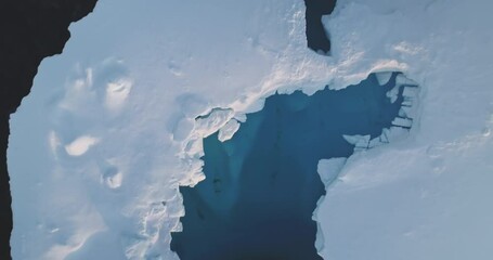 Wall Mural - Melting cave in ice floe snow covered iceberg aerial top down view. Glacier float in polar frozen icy ocean. Ecology, melting ice, climate change global warming. Antarctica travel and exploration